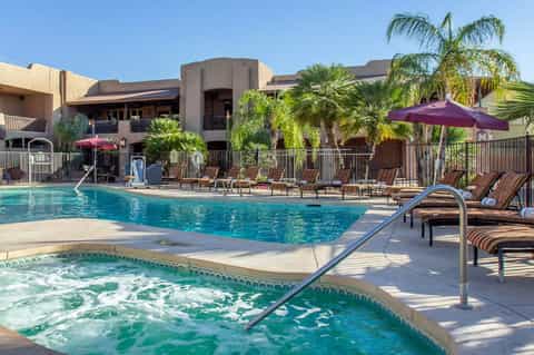 Resort pool with spa tub in foreground, lounge chairs, purple umbrellas, and desert landscaping