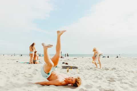 Man doing handstand on sandy beach with ocean and beach volleyball in background