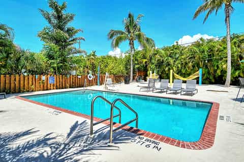 Resort swimming pool with bright blue water, lounge chairs, palm trees, and tropical vegetation