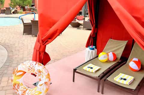 Poolside cabana area with red tent, lounge chairs, beach balls, and resort pool in background