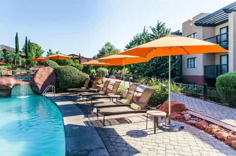 Resort pool area with orange umbrellas, loungers, waterfall, and manicured landscaping