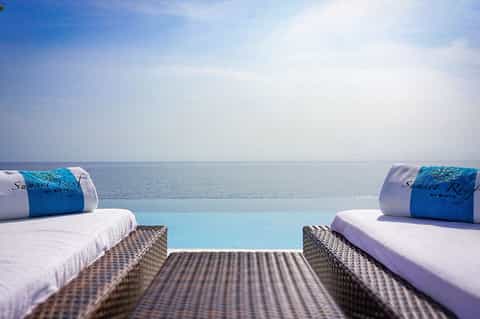 Infinity pool lounge beds with rolled towels and ocean horizon view at Sunset Reef resort