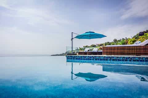 Infinity pool at beach resort with blue umbrella, ocean view, and tropical landscape