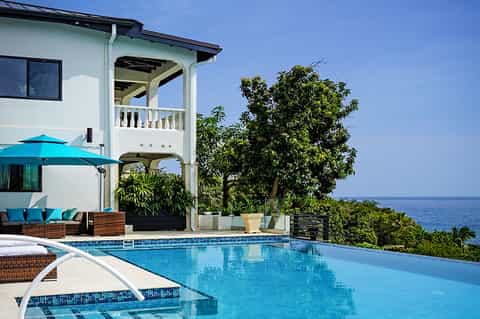 Oceanfront villa with infinity pool, white architecture, turquoise umbrella, and sea views