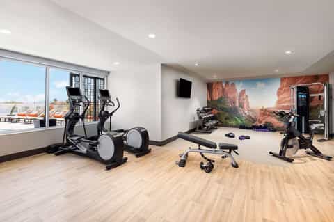 Modern fitness center with elliptical machines, stationary bikes, weights, and desert landscape mural