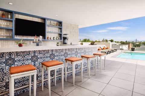 Rooftop bar with patterned tile accent wall, bar seating, and pool area with mountain views