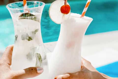 Two refreshing cocktails with mint and citrus garnishes by a turquoise swimming pool
