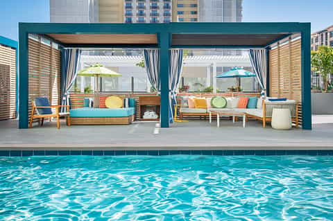 Resort poolside lounge area with turquoise pergolas, wood seating, and colorful cushions
