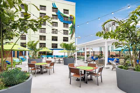 Vibrant rooftop terrace with dining tables, colorful umbrellas, tropical plants, pergola, and city skyline views