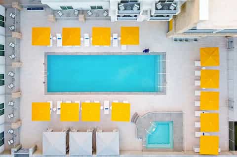 Aerial view of hotel pool deck with bright yellow umbrellas and turquoise swimming pool surrounded by lounge chairs