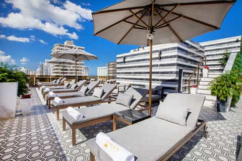 Rooftop lounge with multiple lounge chairs, large umbrellas, patterned pavers, and modern apartment buildings
