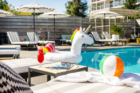 Resort pool area with unicorn float, lounge chairs, umbrellas, and colorful drinks