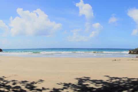 Pristine sandy beach with turquoise ocean water and white clouds in blue sky
