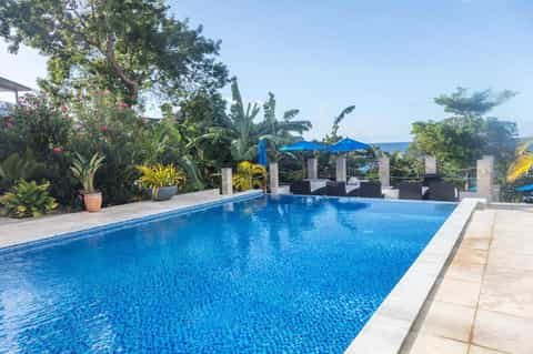 Luxury resort infinity pool overlooking tropical ocean landscape with blue umbrellas and lounge seating
