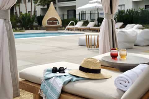 Luxury poolside lounge with cabanas, white furnishings, and teepee-shaped day bed structure