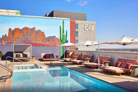 Rooftop pool deck with loungers, umbrellas, and desert mountain mural on modern hotel