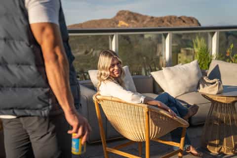 Woman smiling on wicker lounge chair on desert hillside terrace with mountain views