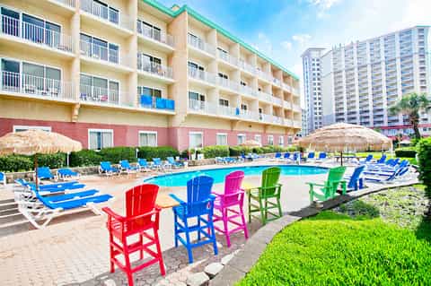 Resort pool area with colorful Adirondack chairs, thatched umbrellas, and multi-story beachfront hotel building