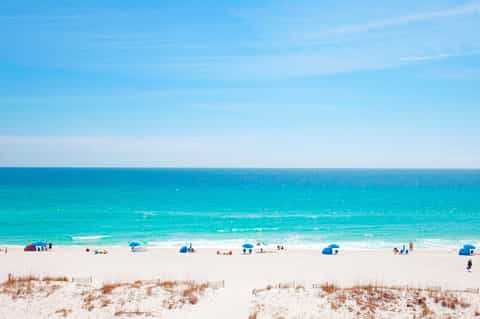 Pristine sandy beach with turquoise ocean, beach umbrellas, and clear blue sky