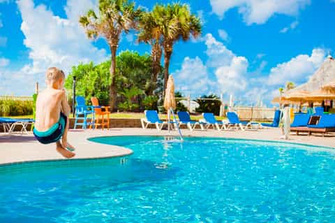 Child about to jump into bright blue resort pool with lounge chairs and palm trees