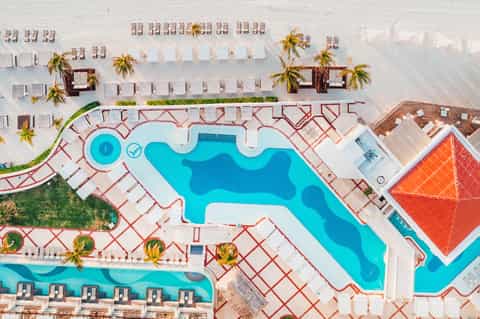 Aerial view of resort pool complex with decorative pavement patterns and organized beach loungers