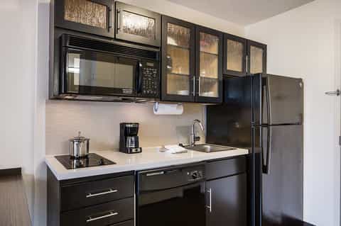 Modern kitchenette with black cabinetry, white countertops, stainless steel appliances