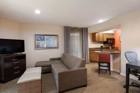 Hotel suite with sofa, kitchenette, TV, desk area, and warm neutral décor
