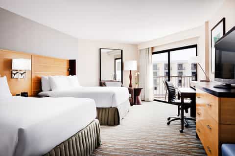 Spacious hotel room with two queen beds, desk, and balcony with city views