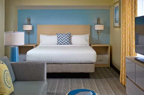 Coastal hotel bedroom with blue accent wall, queen bed, desk area, and chevron patterned pillows