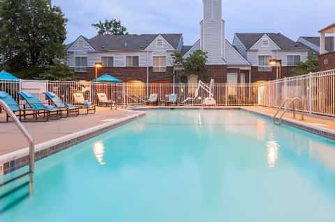 Evening view of hotel pool surrounded by lounge chairs, umbrellas, white railings, and residential buildings