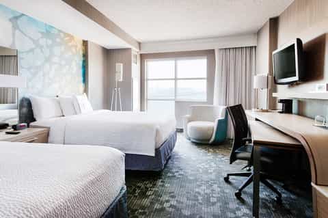 Modern hotel room with two double beds, ocean view balcony, and contemporary furnishings