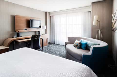 Spacious hotel room with king bed, work desk, sofa, and sliding glass doors to balcony