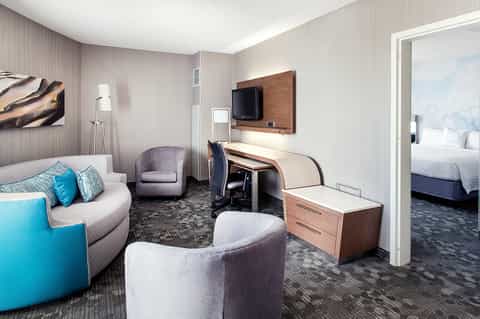 Hotel suite living room with curved sofa, TV, and bedroom doorway