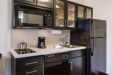 Modern hotel kitchenette with black appliances, white countertops, and glass cabinets