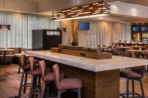 Contemporary hotel lobby featuring large marble-topped bar with wooden base and warm ambient lighting