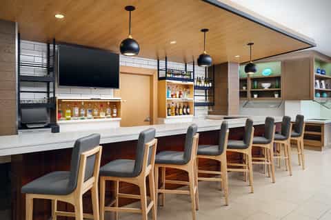 Modern hotel bar and lounge with wooden ceiling, pendant lights, extensive liquor selection, and bar seating