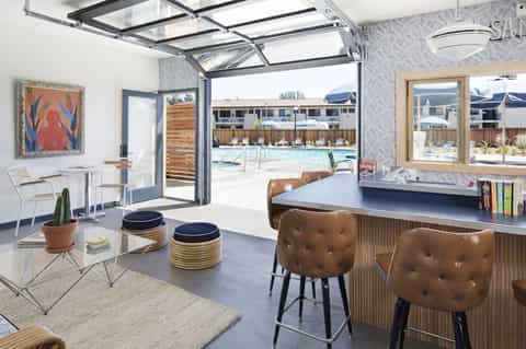 Modern resort lobby with open glass doors overlooking pool, featuring leather bar seating and bright decor
