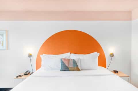 Minimalist hotel bedroom with white bedding and large orange circular headboard accent wall