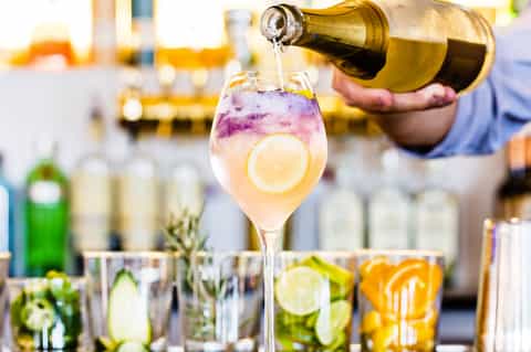 Bartender pouring wine into a glass with purple flower garnish and lemon slice at poolside bar