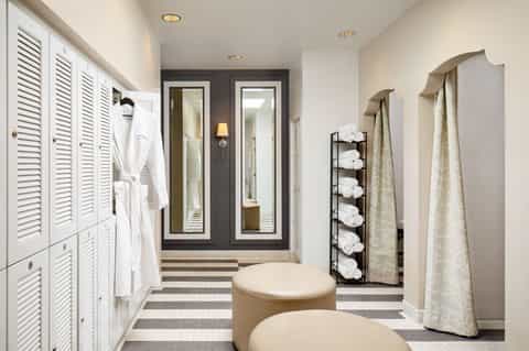 Luxury spa changing room with white louvered closets, striped floor, and rolled towel storage