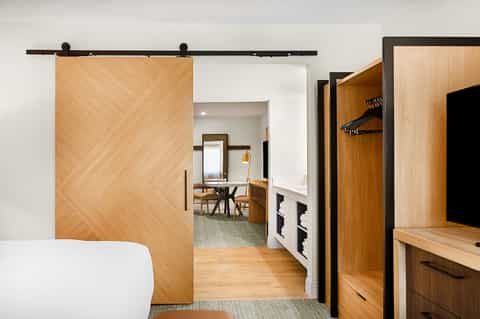 Modern hotel room with sliding barn door, wooden accents, white bed, and contemporary furnishings