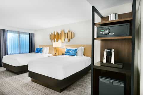 Modern hotel room with two queen beds, blue accent pillows, and wooden headboard