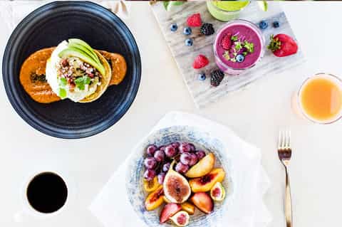Gourmet brunch spread with avocado toast, fruit bowl, smoothie bowls, and beverages on white table