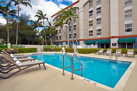 Hotel pool area with dark loungers, palm trees, and multi-story beige building