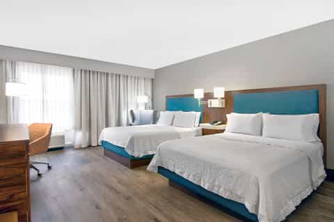 Modern hotel room with two queen beds, turquoise headboards, and floor-to-ceiling windows