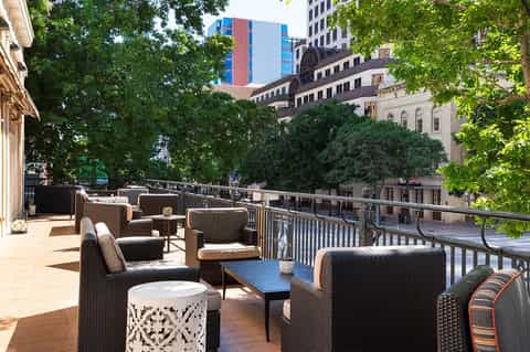 Urban rooftop lounge with brown wicker seating, city skyline views, lush green trees, and modern architecture