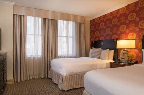 Hotel bedroom with two beds, elegant red patterned wallpaper, and large windows