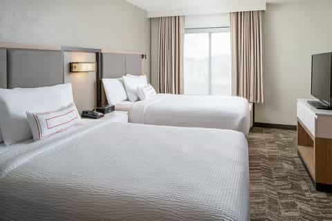 Hotel bedroom with two queen beds, gray headboards, beige bedding, and modern furnishings
