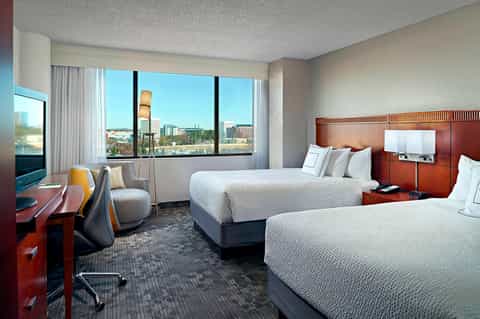 Hotel bedroom with two queen beds, red wood headboards, city views, and modern amenities