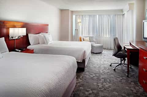 Hotel room with two queen beds, red headboard, seating area, and floor-to-ceiling windows